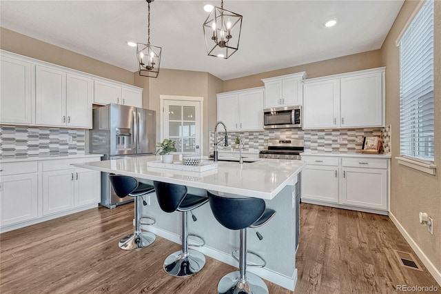 kitchen featuring visible vents, appliances with stainless steel finishes, wood finished floors, light countertops, and a sink