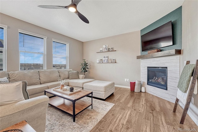 living room with a fireplace, ceiling fan, a textured ceiling, wood finished floors, and baseboards