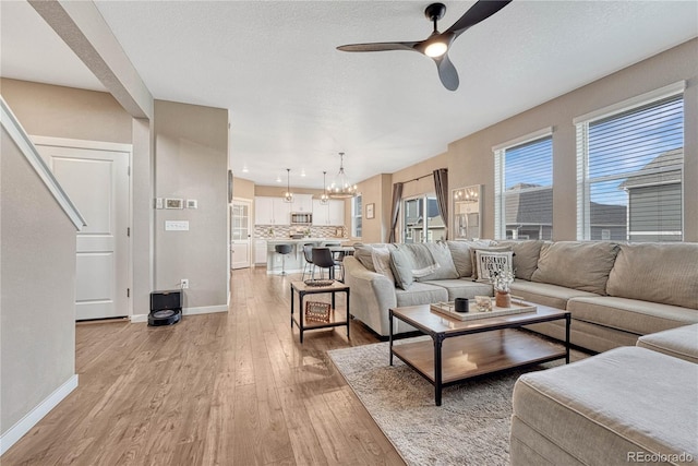 living room with light wood-style floors, baseboards, a textured ceiling, and ceiling fan with notable chandelier