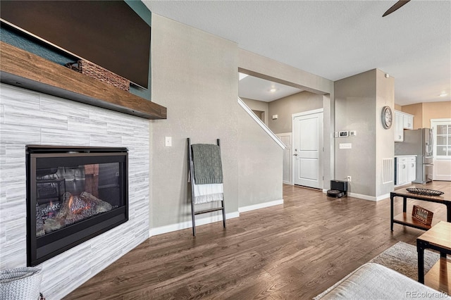 living room with stairs, a glass covered fireplace, wood finished floors, and baseboards