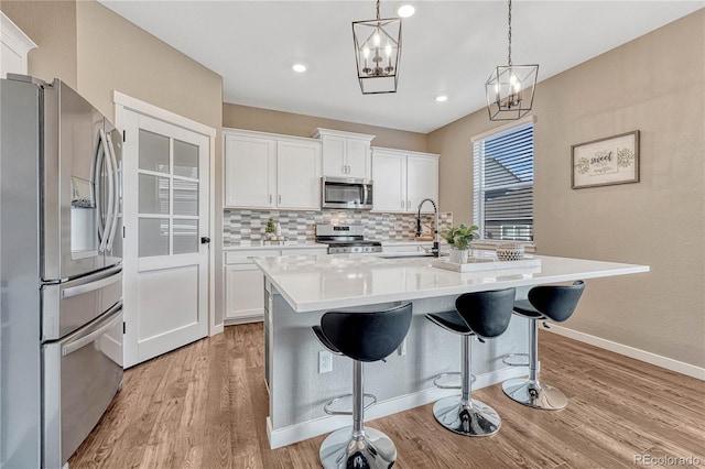 kitchen featuring light wood finished floors, decorative backsplash, appliances with stainless steel finishes, light countertops, and a sink