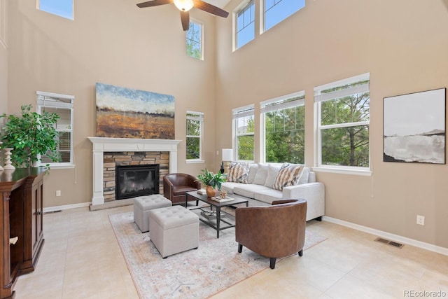 living room with a high ceiling, a stone fireplace, ceiling fan, light tile patterned floors, and baseboards