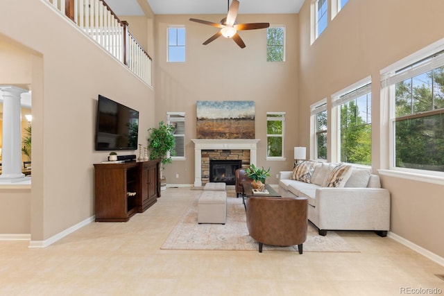 living area featuring a towering ceiling, plenty of natural light, decorative columns, ceiling fan, and baseboards