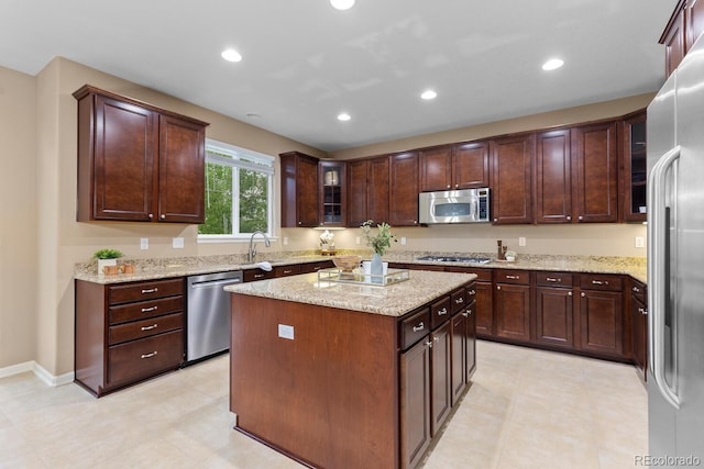 kitchen featuring appliances with stainless steel finishes, a kitchen island, light stone countertops, glass insert cabinets, and recessed lighting