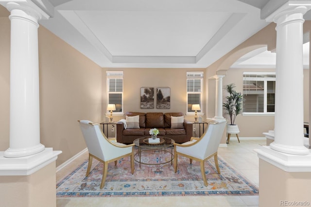 tiled living room featuring decorative columns, a raised ceiling, arched walkways, and baseboards