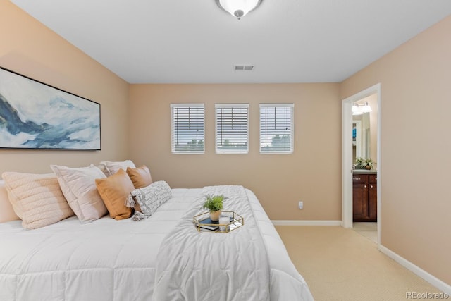 bedroom with light colored carpet, baseboards, and ensuite bath