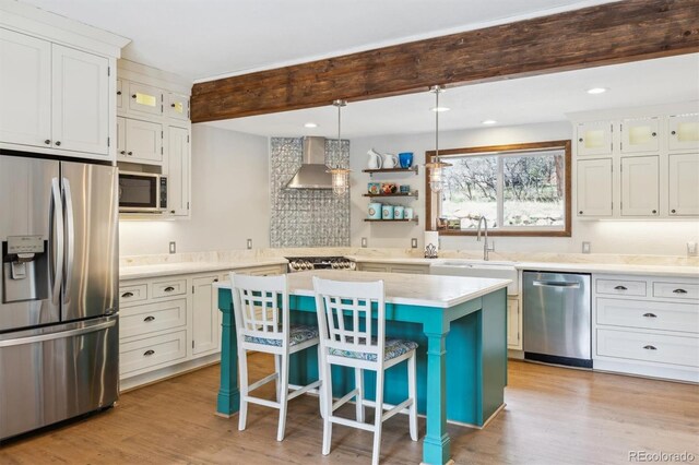 7317 Fremont Pl, Larkspur, CO 80118 - kitchen with stainless steel appliances, a breakfast bar, light countertops, wall chimney range hood, and light wood-style floors