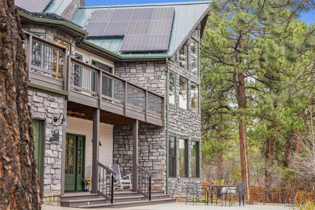 7317 Fremont Pl, Larkspur, CO 80118 - rear view of house with metal roof, roof mounted solar panels, stone siding, and a balcony