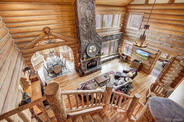 living room with a towering ceiling, hardwood / wood-style flooring, a stone fireplace, and log walls