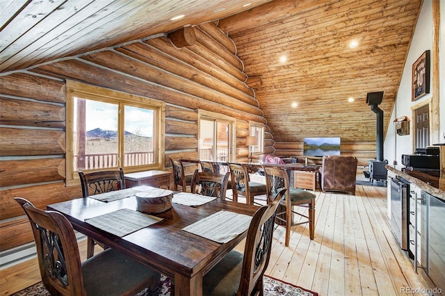 dining area with rustic walls, light hardwood / wood-style flooring, wood ceiling, a wood stove, and high vaulted ceiling