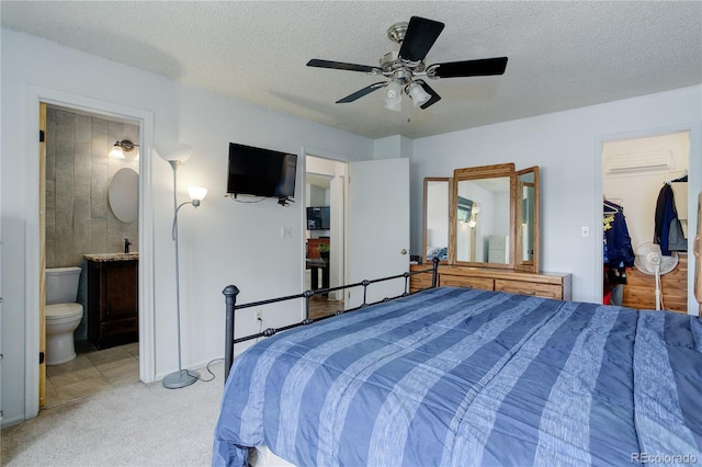 bedroom featuring a walk in closet, light colored carpet, ensuite bath, a textured ceiling, and a closet