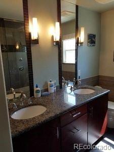 full bath with a stall shower, double vanity, toilet, and a sink