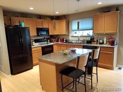 kitchen featuring backsplash, light wood finished floors, a breakfast bar, a center island, and black appliances
