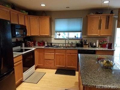 kitchen with stone counters, backsplash, a sink, light wood-style flooring, and black appliances