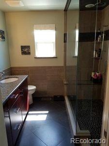 full bathroom with tile walls, a wainscoted wall, toilet, vanity, and a stall shower