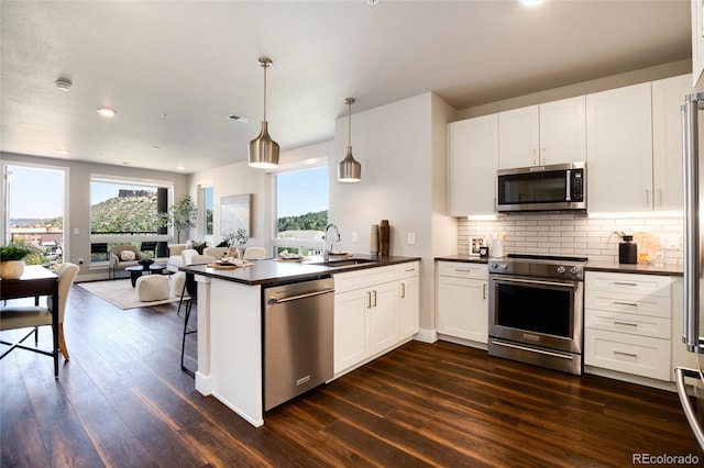 kitchen with white cabinets, dark countertops, open floor plan, a peninsula, and stainless steel appliances