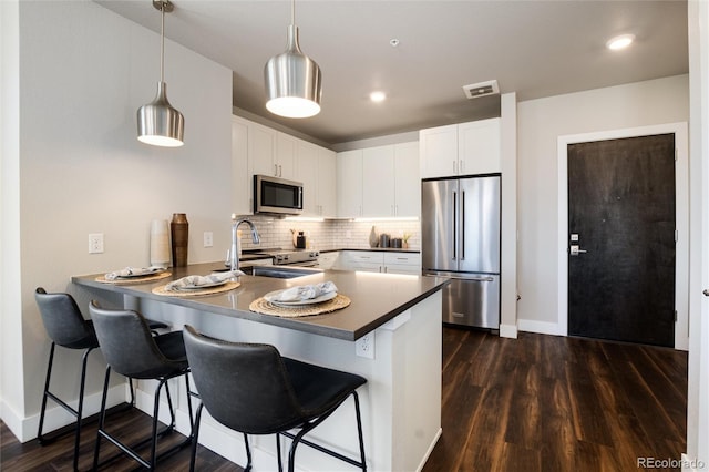 kitchen with stainless steel appliances, pendant lighting, white cabinetry, and a peninsula