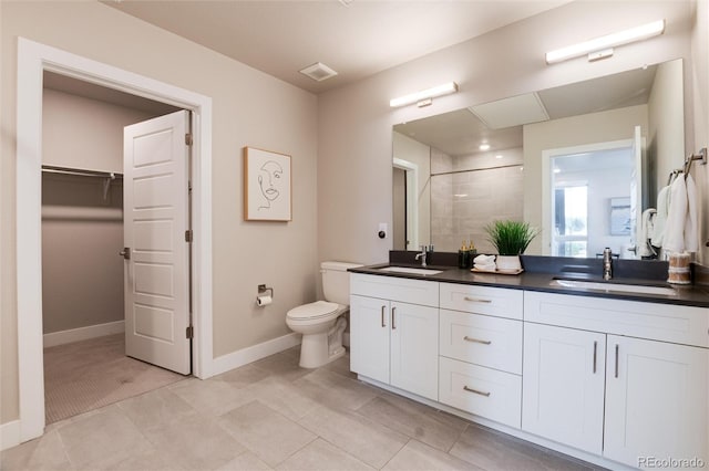 bathroom featuring toilet, a sink, baseboards, a spacious closet, and double vanity