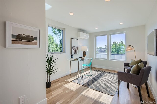 sitting room with plenty of natural light, a wall unit AC, and light hardwood / wood-style flooring