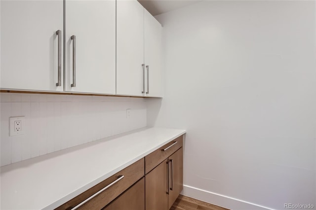 bar with backsplash, white cabinetry, and light hardwood / wood-style flooring