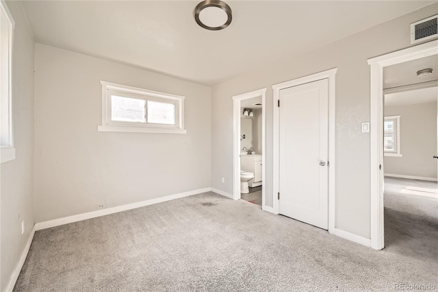 unfurnished bedroom featuring ensuite bathroom, multiple windows, and light colored carpet