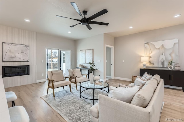 living area with light wood-style floors, a large fireplace, recessed lighting, a ceiling fan, and baseboards
