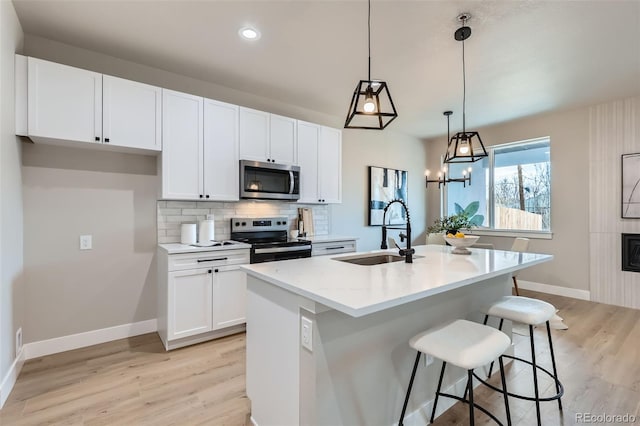 kitchen with baseboards, light wood-type flooring, white cabinetry, a sink, and appliances with stainless steel finishes