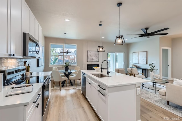kitchen featuring open floor plan, white cabinetry, a sink, light wood-style flooring, and appliances with stainless steel finishes