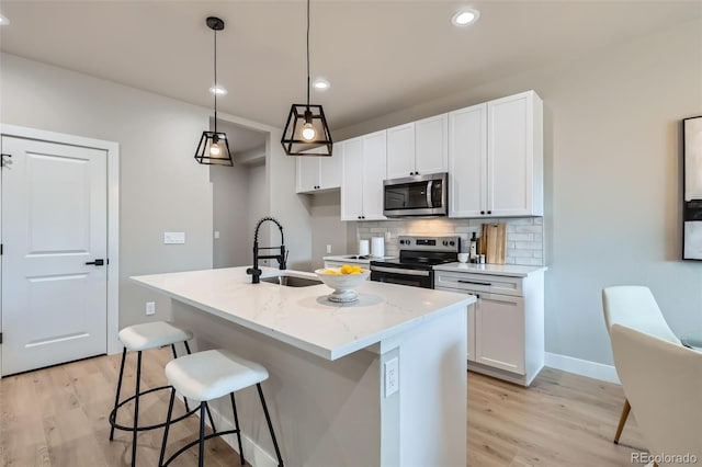 kitchen featuring backsplash, a sink, white cabinets, light wood finished floors, and stainless steel appliances