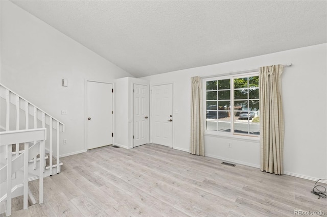 spare room with lofted ceiling, stairs, wood finished floors, and visible vents