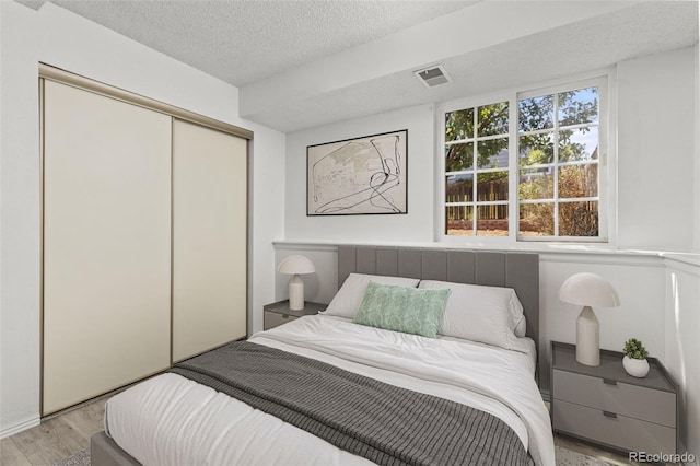 bedroom with light wood-style flooring, a textured ceiling, visible vents, and a closet