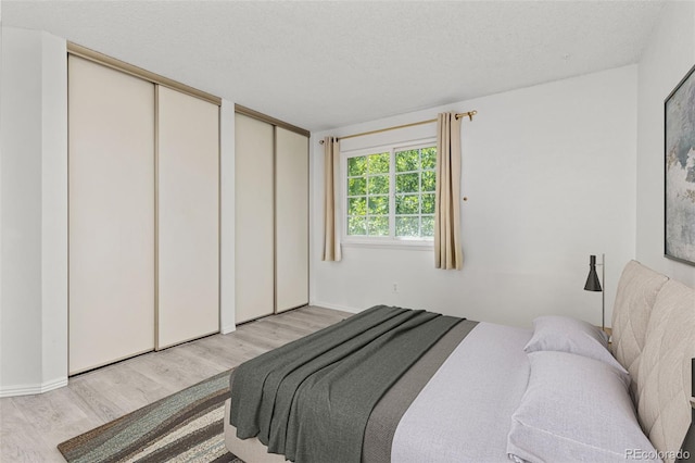 bedroom featuring light wood-style floors, a textured ceiling, and multiple closets