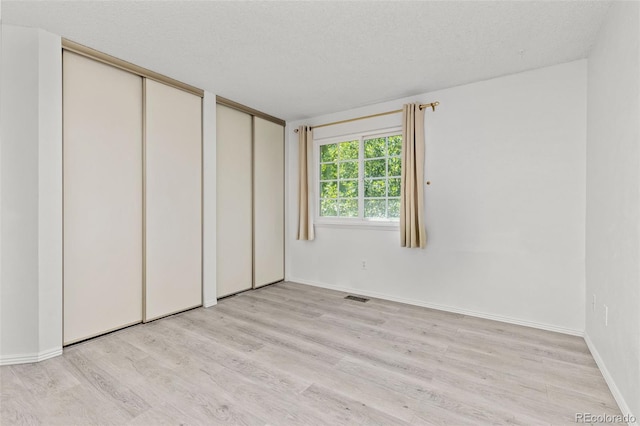 unfurnished bedroom featuring light wood finished floors, two closets, visible vents, a textured ceiling, and baseboards