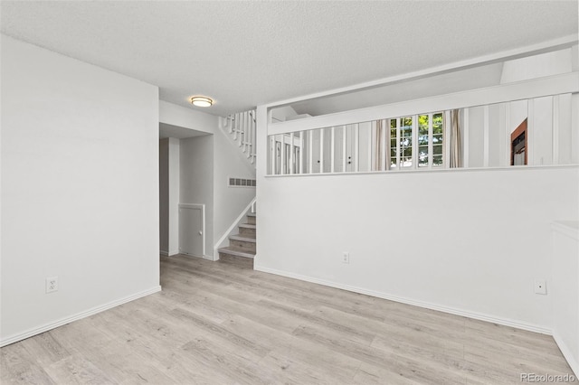 empty room featuring visible vents, stairway, a textured ceiling, wood finished floors, and baseboards