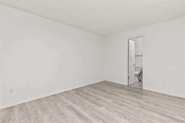 empty room featuring a textured ceiling, light wood-style flooring, and baseboards