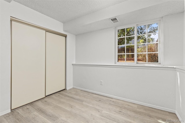 unfurnished bedroom featuring baseboards, visible vents, wood finished floors, a textured ceiling, and a closet