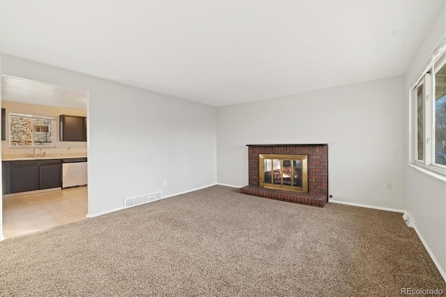 unfurnished living room with a brick fireplace, light colored carpet, and sink