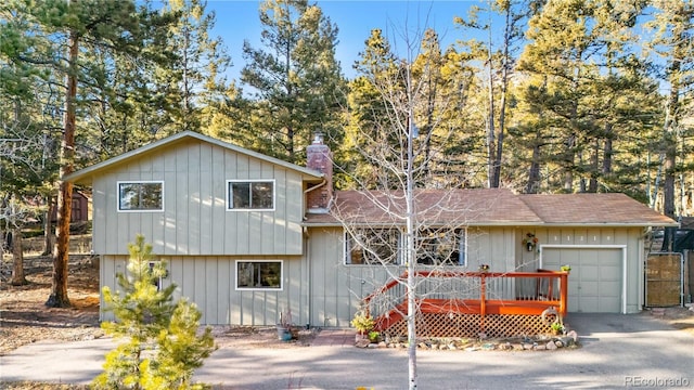 split level home featuring a garage, driveway, board and batten siding, and a chimney