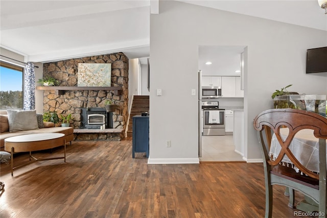 living area with a wood stove, vaulted ceiling with beams, wood finished floors, and baseboards