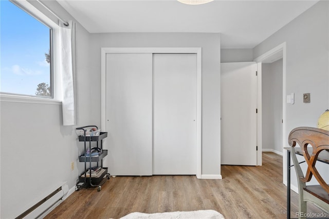 bedroom featuring a closet, baseboards, baseboard heating, and wood finished floors