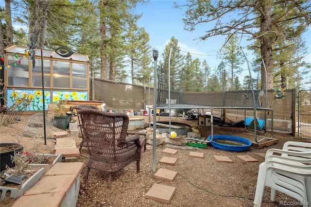 exterior space featuring a greenhouse, a trampoline, an outdoor structure, and fence