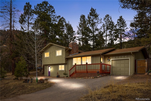 split level home featuring driveway, a chimney, an attached garage, and board and batten siding