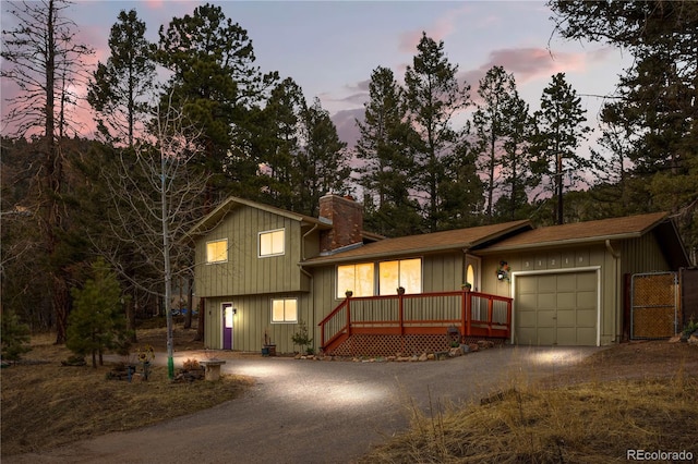 split level home with aphalt driveway, an attached garage, board and batten siding, and a chimney