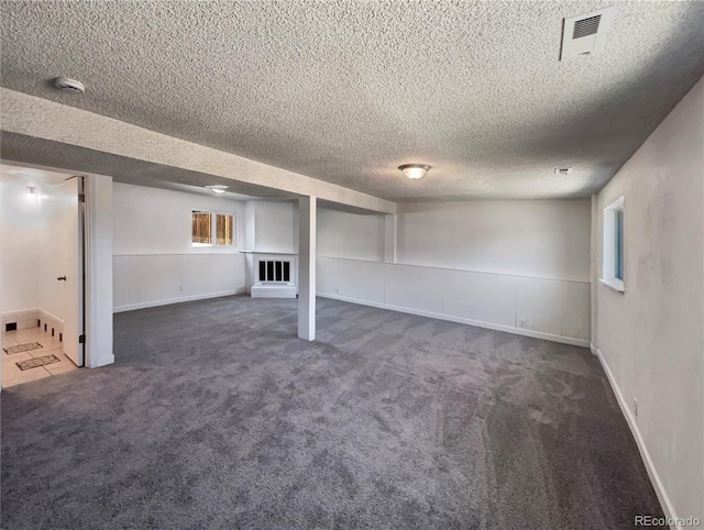 below grade area with a textured ceiling, carpet flooring, visible vents, and baseboards