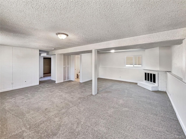 finished basement featuring carpet flooring, a fireplace, a textured ceiling, and baseboards