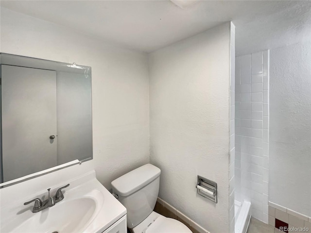 bathroom featuring a textured wall, tiled shower, vanity, and toilet