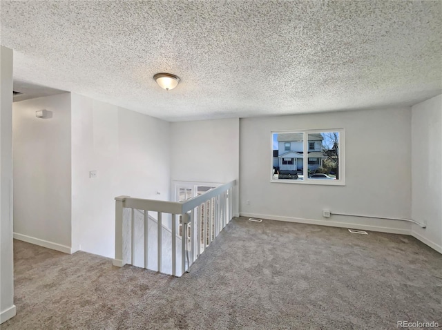 spare room featuring a textured ceiling, carpet flooring, visible vents, and baseboards