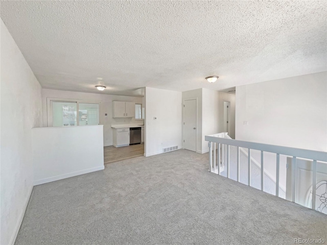 spare room with light carpet, a textured ceiling, visible vents, and baseboards