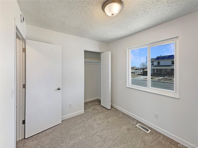 unfurnished bedroom featuring a closet, visible vents, light carpet, a textured ceiling, and baseboards