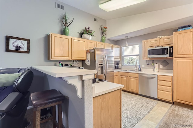 kitchen featuring kitchen peninsula, light brown cabinets, stainless steel appliances, and a breakfast bar